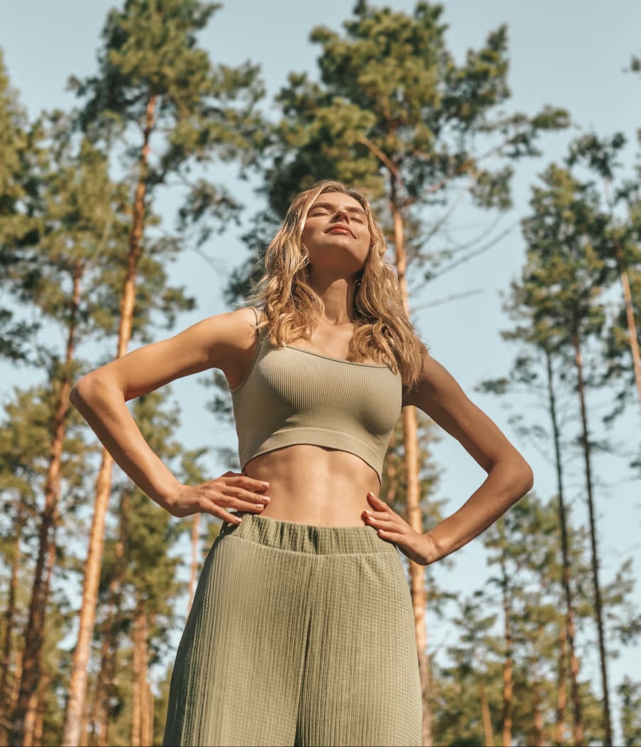 Woman standing outdoors among tall pine trees